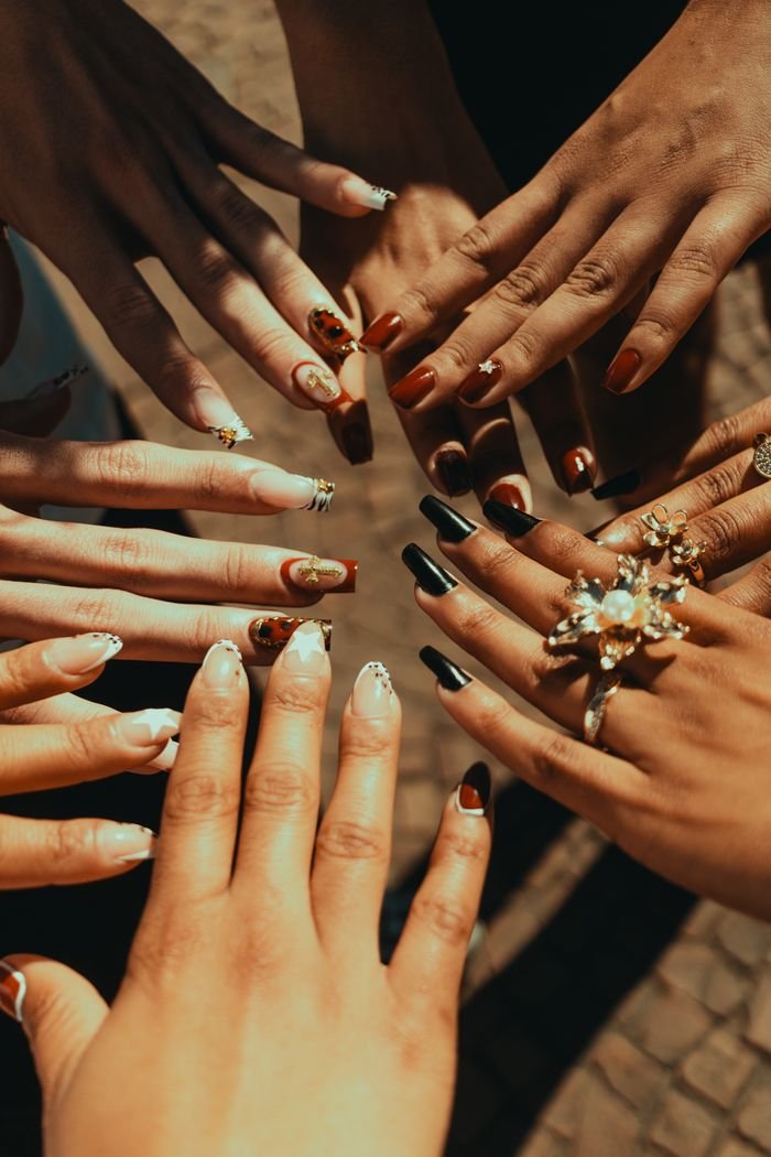 A circle of diverse hands showcasing elaborate and colorful nail art in an outdoor setting.